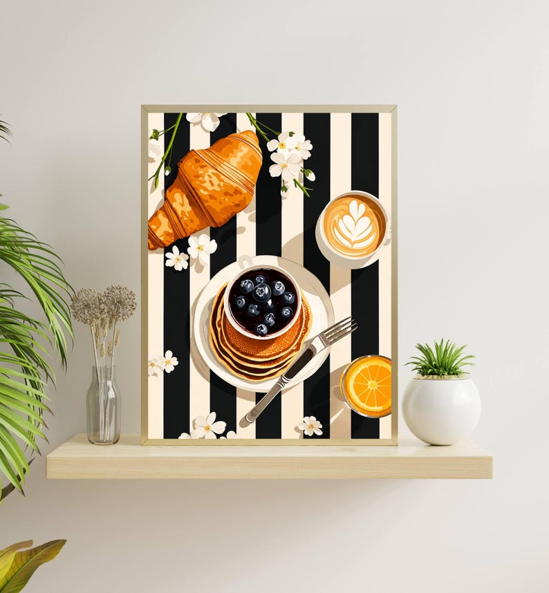 Pu&ograve; includere: Una stampa artistica incorniciata raffigurante una scena di colazione con un croissant dorato, una pila di pancake con mirtilli, una tazza di caff&egrave; con latte art e un bicchiere di succo d'arancia su uno sfondo a righe verticali bianche e nere.