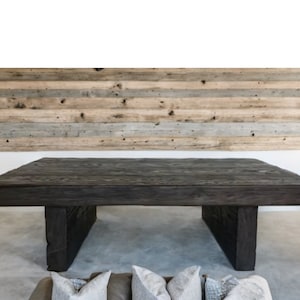 May include: A large, dark wood coffee table with a thick, rectangular top and two chunky, square legs. The table is made of reclaimed wood and has a rustic, industrial look.