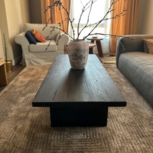May include: A dark wood coffee table with a black base sits on a patterned rug in a living room. A vase with a floral design holds a dried branch with twigs.