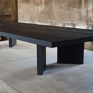 May include: A long, black wooden table with a rectangular top and four legs. The table is made of solid wood and has a natural, rustic finish.
