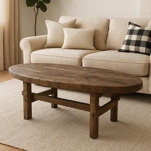 Könnte beinhalten: Ein ovaler Couchtisch aus dunklem Holz steht auf einem beigefarbenen Teppich vor einem cremefarbenen Sofa mit Kissen. Ein gerahmtes Landschaftsbild hängt an der Wand. Wohnzimmer-Atmosphäre.