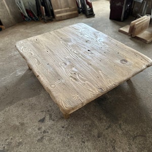 May include: A rustic wooden coffee table with a natural wood finish and a rectangular shape. The table has a rough, uneven surface and appears to be made from reclaimed wood.