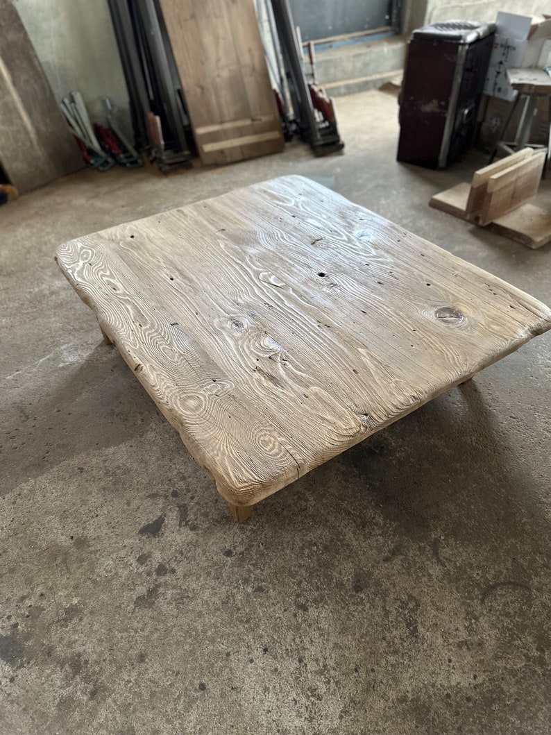 May include: A rustic wooden coffee table with a natural wood finish and a rectangular shape. The table has a rough, uneven surface and appears to be made from reclaimed wood.