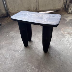 May include: A black wooden stool with a curved top and four legs. The stool has a natural wood grain pattern visible on the top.