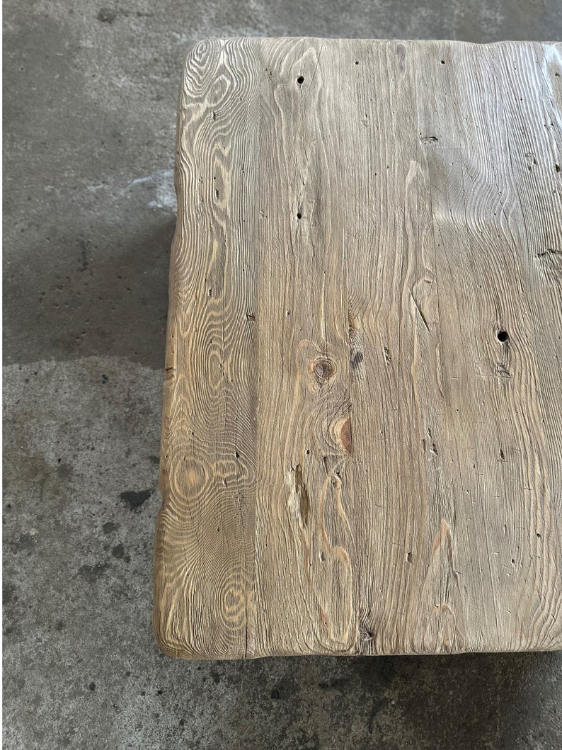 May include: A close-up of a rustic wooden table top with a natural wood grain pattern. The wood is light brown with a weathered finish.