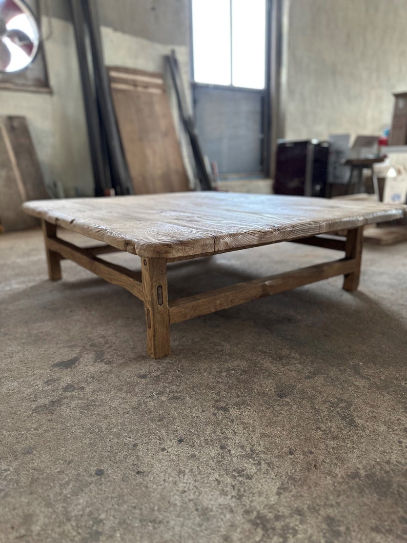 May include: A rustic wooden coffee table with a square top and a lower shelf. The table is made of natural wood with a weathered finish.