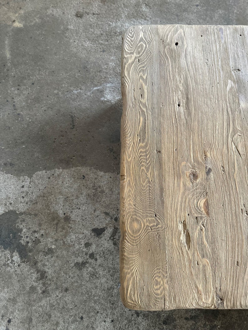 May include: Close-up of a rustic wooden table top with a natural wood grain pattern and knots. The wood is a light brown colour with a weathered finish.