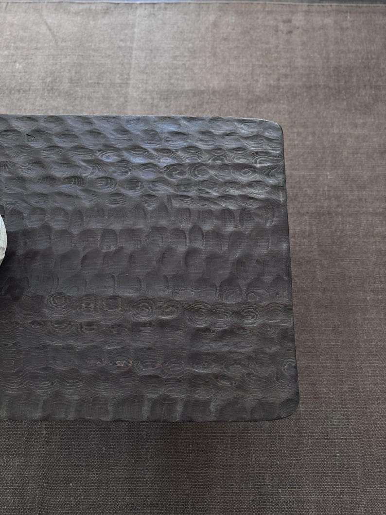 Op de afbeelding: Een donkerbruine houten salontafel met een getextureerd oppervlak. De tafel heeft een rechthoekige vorm en een gladde, gepolijste afwerking.