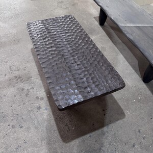 Op de afbeelding: Een donkerbruine houten salontafel met een getextureerd oppervlak. De tafel is rechthoekig en gemaakt van massief hout.