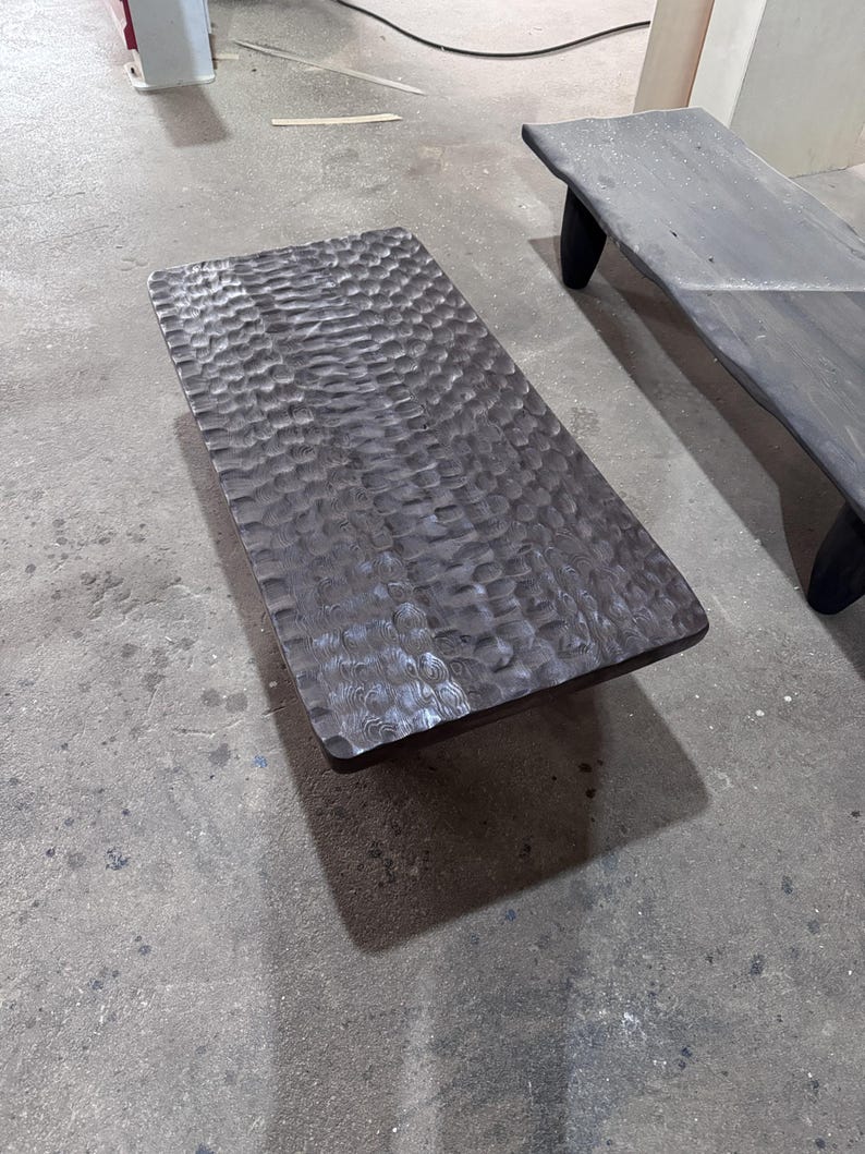 Op de afbeelding: Een donkerbruine houten salontafel met een getextureerd oppervlak. De tafel is rechthoekig en gemaakt van massief hout.