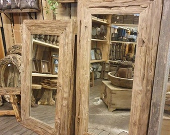 Op de afbeelding: Twee grote rechthoekige spiegels met rustieke, natuurlijke houten frames. De spiegels leunen tegen een houten muur en weerspiegelen een kamer vol houten meubels en planken. De frames hebben een ruwe, getextureerde uitstraling.