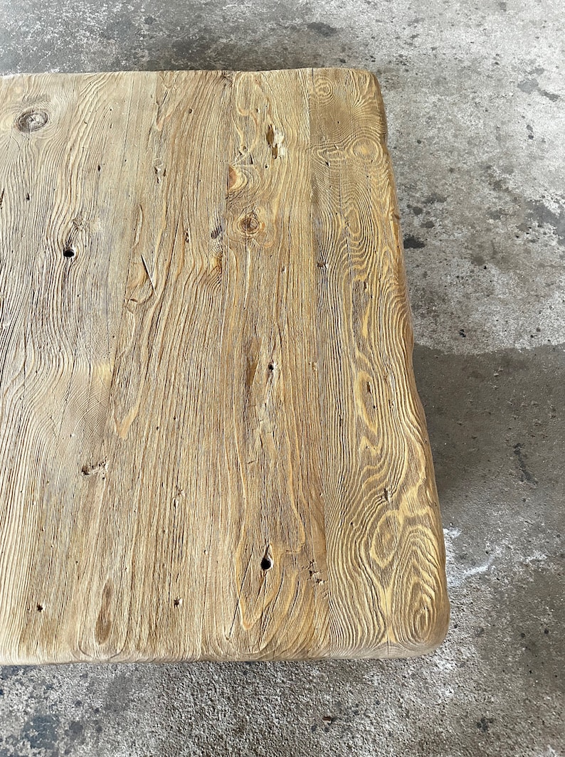 May include: A close-up of a rustic wooden table top with a natural wood grain pattern and knots. The wood has a light brown colour and a rough texture.