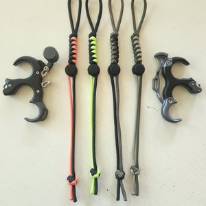 May include: Five different colored paracord bow release aids. The release aids are black with different colored accents. The release aids are tied with a knot at the bottom.