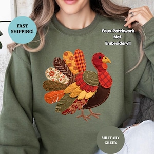 May include: A military green crewneck sweatshirt featuring a central graphic of a turkey with a faux patchwork design. The turkey is composed of various autumn-colored patterns including plaid, floral, and solid textures. Text reads Faux Patchwork Not Embroidery.