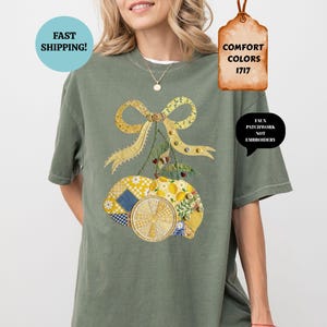 May include: A moss green t-shirt featuring a lemon design with a yellow bow and patchwork details. The design includes the text "FAUX PATCHWORK NOT EMBROIDERY" and "COMFORT COLORS 1717". The shirt has a relaxed fit.