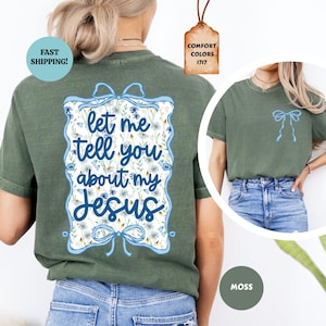 May include: Moss green t-shirt with a floral design and the text "Let me tell you about my Jesus" in blue script. The shirt features a light blue bow design on the back and a smaller bow on the front.