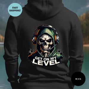 May include: Black hoodie featuring a skull wearing a headset and a green hood. The graphic includes the text "GET ON MY LEVEL" in white. The hoodie is a solid black color.