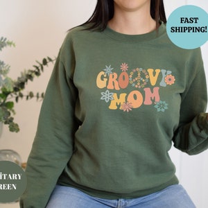 May include: Green sweatshirt with the text "Groovy Mom" in colorful retro lettering with peace signs and flowers.