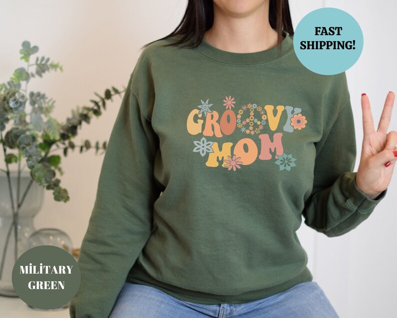 May include: Green sweatshirt with the text "Groovy Mom" in colorful retro lettering with peace signs and flowers.