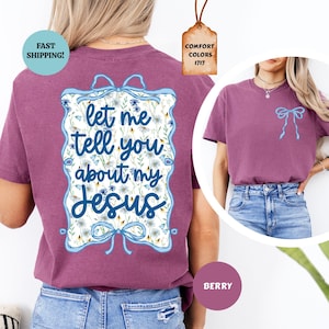 May include: Berry-colored t-shirt with the text "let me tell you about my Jesus" in a floral design. The shirt has a light blue bow on the front and a tag that says "Comfort Colors 1717".
