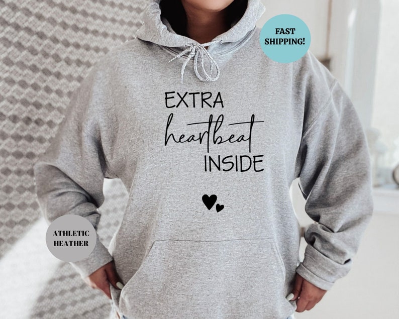 Pode incluir: Camisola de moletom cinza com capuz com o texto "EXTRA heartbeat INSIDE" e dois cora&ccedil;&otilde;es pretos abaixo do texto. A camisola &eacute; feita de material heather atl&eacute;tico.