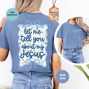 May include: Blue jean-colored t-shirt with the text "let me tell you about my Jesus" in a decorative floral frame. The shirt has a bow design on the front and back. The shirt is a Comfort Colors 1717.