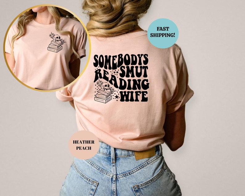 May include: A pink t-shirt with the text "Somebody's Smut Reading Wife" in black, with a skull and stack of books graphic. The shirt is shown on a model wearing blue jeans.