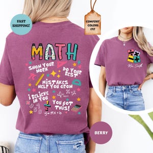 Puede incluir: Camiseta de color bayas con un dise&ntilde;o tem&aacute;tico de matem&aacute;ticas. La parte posterior presenta la palabra "MATH" en letras coloridas, junto con s&iacute;mbolos matem&aacute;ticos y frases como "Show Your Work" y "You Got This!". La parte delantera tiene un peque&ntilde;o dise&ntilde;o de s&iacute;mbolo matem&aacute;tico.
