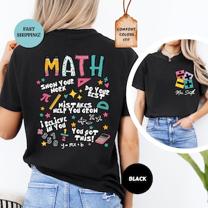 Puede incluir: Camiseta negra con un gr&aacute;fico colorido de "MATH" en la espalda, con s&iacute;mbolos matem&aacute;ticos y frases como "Show Your Work" y "You Got This!". Un gr&aacute;fico m&aacute;s peque&ntilde;o con s&iacute;mbolos matem&aacute;ticos y "Mrs. Smith" est&aacute; en la parte delantera.