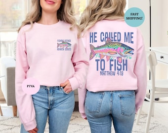 Peut inclure: Sweat-shirt rose clair avec un motif de poisson coloré au dos, accompagné du texte "He Called Me To Fish" et "Matthew 4:19." L'avant présente un motif de poisson plus petit et les mots "Fishing License Heaven Issued."