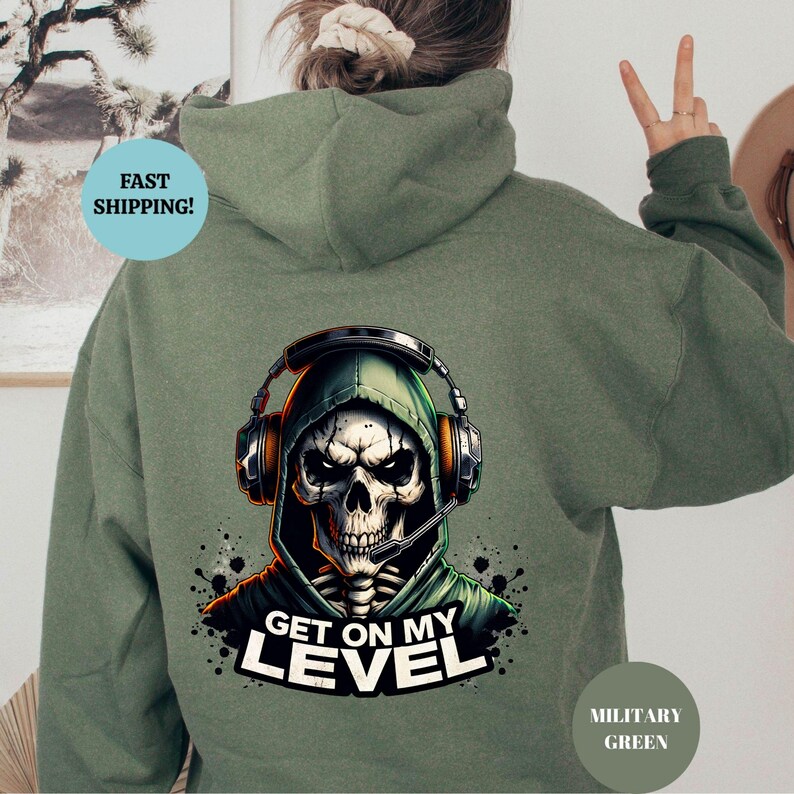 May include: Military green hoodie featuring a skull wearing a headset and a green hood. The graphic includes the text "GET ON MY LEVEL" in white. The hoodie is a solid color with a drawstring hood.