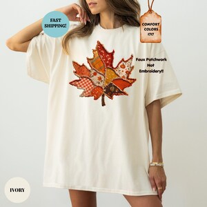 May include: An ivory t-shirt featuring a large, central maple leaf graphic composed of various orange, brown, and yellow patterned fabric segments. The design includes text stating "Faux Patchwork Not Embroidery!!" and "COMFORT COLORS 1717".