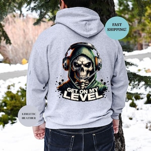 May include: Athletic heather gray hoodie with a graphic of a skull wearing a headset and a green hood. The text "GET ON MY LEVEL" is below the skull. The hoodie is shown from the back.