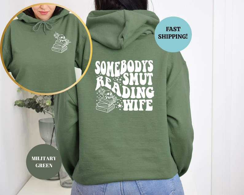May include: A green hooded sweatshirt with the text "Somebody's Smut Reading Wife" printed on the back in white. The text is in a retro font style with stars and a stack of books.
