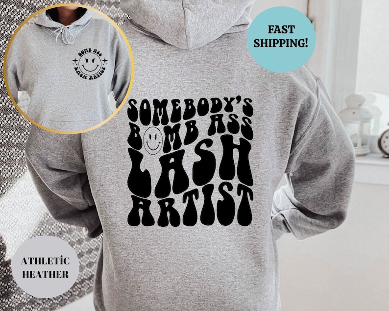 May include: Gray hoodie with a black graphic that says "Somebody's Bomb Ass Lash Artist" in a retro font. The graphic includes a smiley face.