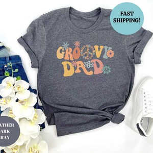 May include: Heather dark gray t-shirt with the text "Groovy Dad" in colorful retro lettering with flower accents.