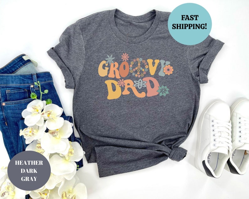 May include: Heather dark gray t-shirt with the text "Groovy Dad" in colorful retro lettering with flower accents.