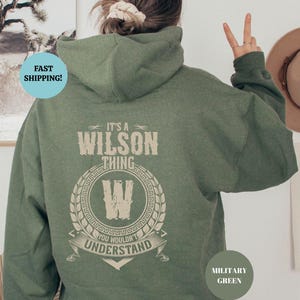 May include: A green hooded sweatshirt with the text "It's a Wilson Thing You Wouldn't Understand" and a stylized "W" in a circle. The sweatshirt is a military green color.