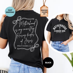 May include: Black t-shirt with white text that reads "Motherhood is my ministry Raising disciples of Jesus Proverbs 22:6". The text is in a decorative frame with a bow at the bottom. The back of the shirt has white text that reads "Motherhood is Kingdom work Proverbs 22:6" with a cross symbol.