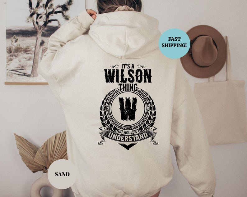 May include: A cream-colored hooded sweatshirt with black text that reads "It's a Wilson thing. You wouldn't understand." The text is surrounded by a black wreath with a black "W" in the center.