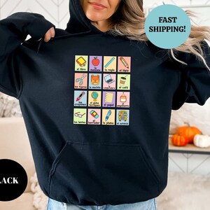 May include: Black hoodie with a graphic of a grid of colorful squares featuring Spanish words and illustrations of school supplies. The text "FAST SHIPPING!" is in a blue circle at the top right corner of the image.