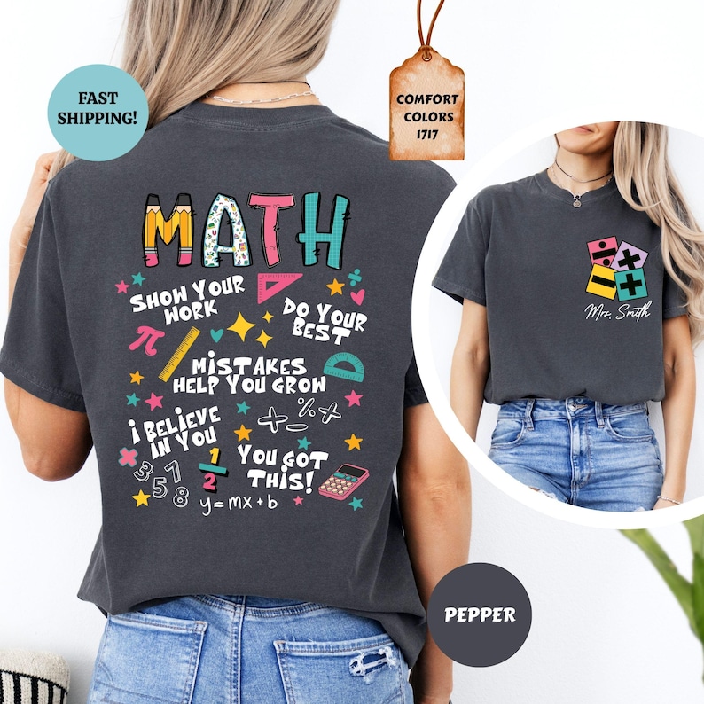 Puede incluir: Camiseta gris oscuro con un gr&aacute;fico "MATH" colorido en la espalda, con s&iacute;mbolos matem&aacute;ticos y frases como "Show Your Work" y "You Got This!". Un gr&aacute;fico m&aacute;s peque&ntilde;o con s&iacute;mbolos matem&aacute;ticos est&aacute; en la parte delantera.