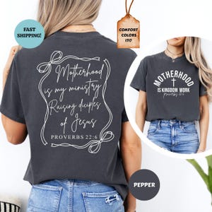 May include: Two charcoal grey t-shirts with white text. The back of one shirt says "Motherhood is my ministry Raising disciples of Jesus Proverbs 22:6". The front of the other shirt says "Motherhood is Kingdom Work Proverbs 22:6".