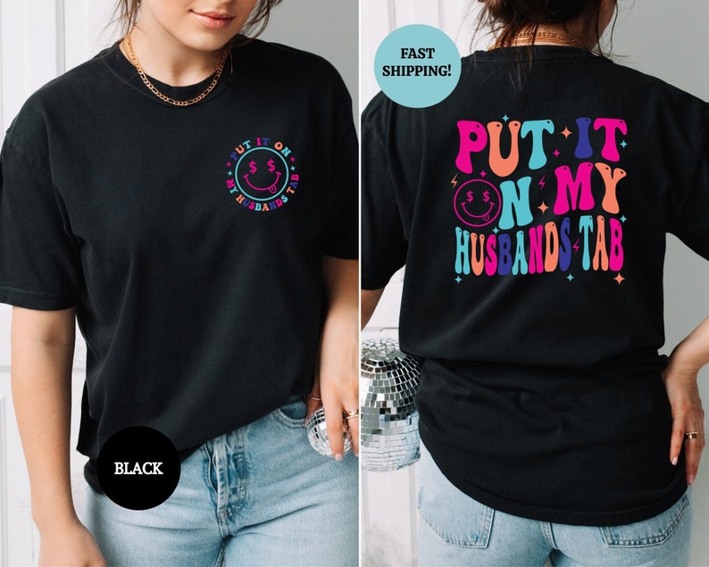 May include: Black t-shirt with a colorful graphic that says "Put it on my husband's tab" with a smiley face and dollar signs.