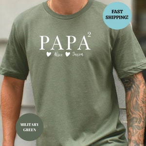 Op de afbeelding: Een groen T-shirt met de tekst "PAPA²" en twee harten met de namen "Alice" en "Jason" erop gedrukt.