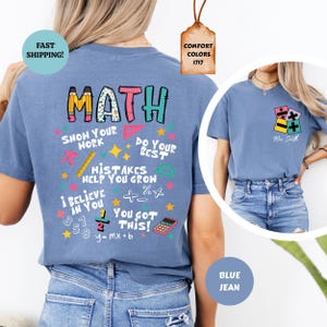 Puede incluir: Una camiseta azul vaquera con la palabra "MATH" en letras coloridas. La parte posterior de la camiseta presenta gr&aacute;ficos y frases relacionadas con las matem&aacute;ticas como "Show Your Work" y "Mistakes Help You Grow". Una imagen m&aacute;s peque&ntilde;a en la parte delantera muestra s&iacute;mbolos matem&aacute;ticos.