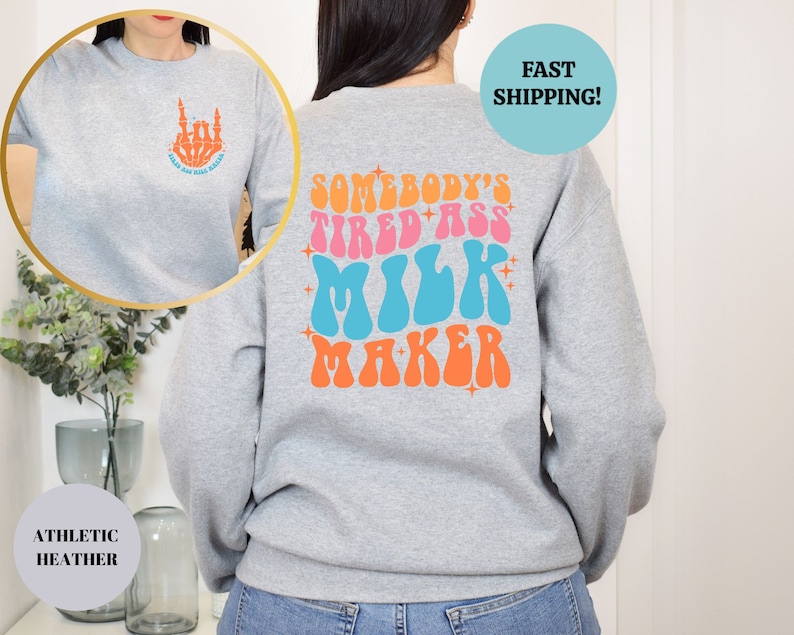 Pu&ograve; includere: Felpa grigia con una grafica in stile retr&ograve; sul retro che dice "Somebody's Tired Ass Milk Maker" in rosa, blu e arancione. La parte anteriore della felpa ha una piccola grafica di una mano scheletrica che fa il gesto rock and roll.