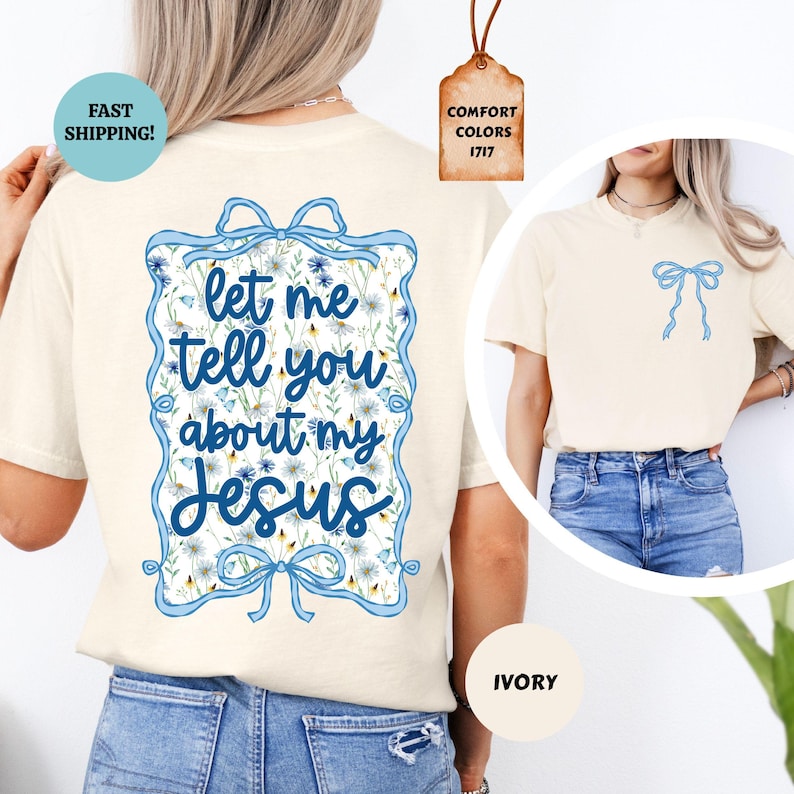 May include: Ivory-colored t-shirt with a blue bow graphic on the front and a larger design on the back. The back design features the text "let me tell you about my Jesus" in a blue frame with floral accents. The shirt has short sleeves.