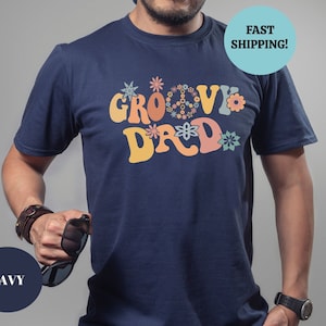 May include: A navy blue t-shirt with a retro-style graphic that says "Groovy Dad" in colorful letters surrounded by flowers.