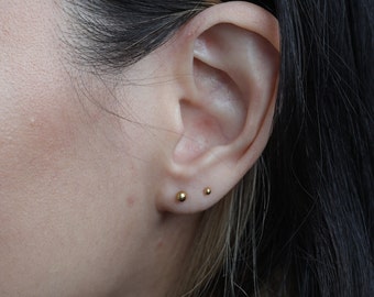 May include: Close-up of a person's ear with two small gold stud earrings.